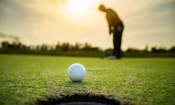 golf ball near hole and golfer blurred in background