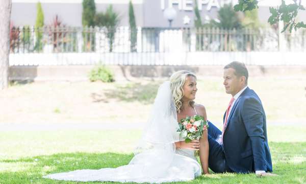 Bride and groom sat in the grass with the park hotel in background